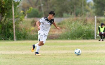 Teen soccer player dribbles the ball on the field during a competitive match.