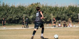 Teenager playing soccer outdoors on a sunny day with teammates.