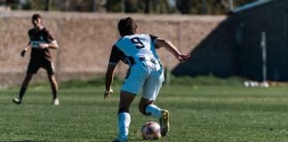 Soccer player dribbles during a match on a sunlit outdoor field with dynamic motion.