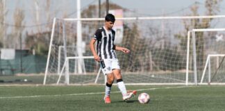 A teenage soccer player dribbles the ball on an outdoor football field during the day.