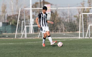 A teenage soccer player dribbles the ball on an outdoor football field during the day.