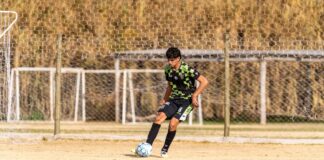 A teenager in a green camo jersey focusing on the soccer ball during practice outdoors.