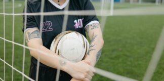 Close-up of a tattooed soccer player holding a ball on an outdoor field.