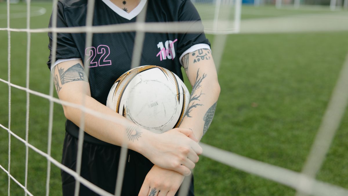 Close-up of a tattooed soccer player holding a ball on an outdoor field. Close-up of a tattooed soccer player holding a ball on an outdoor field.