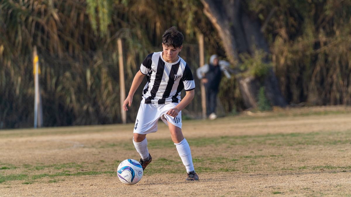 Young soccer player in a black and white uniform dribbles the ball on a grassy field during a sunny day. Young soccer player in a black and white uniform dribbles the ball on a grassy field during a sunny day.