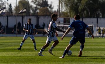 Players compete in a dynamic soccer match under clear skies on a grassy field.