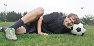 Teen soccer player smiling on grass field resting with a soccer ball.
