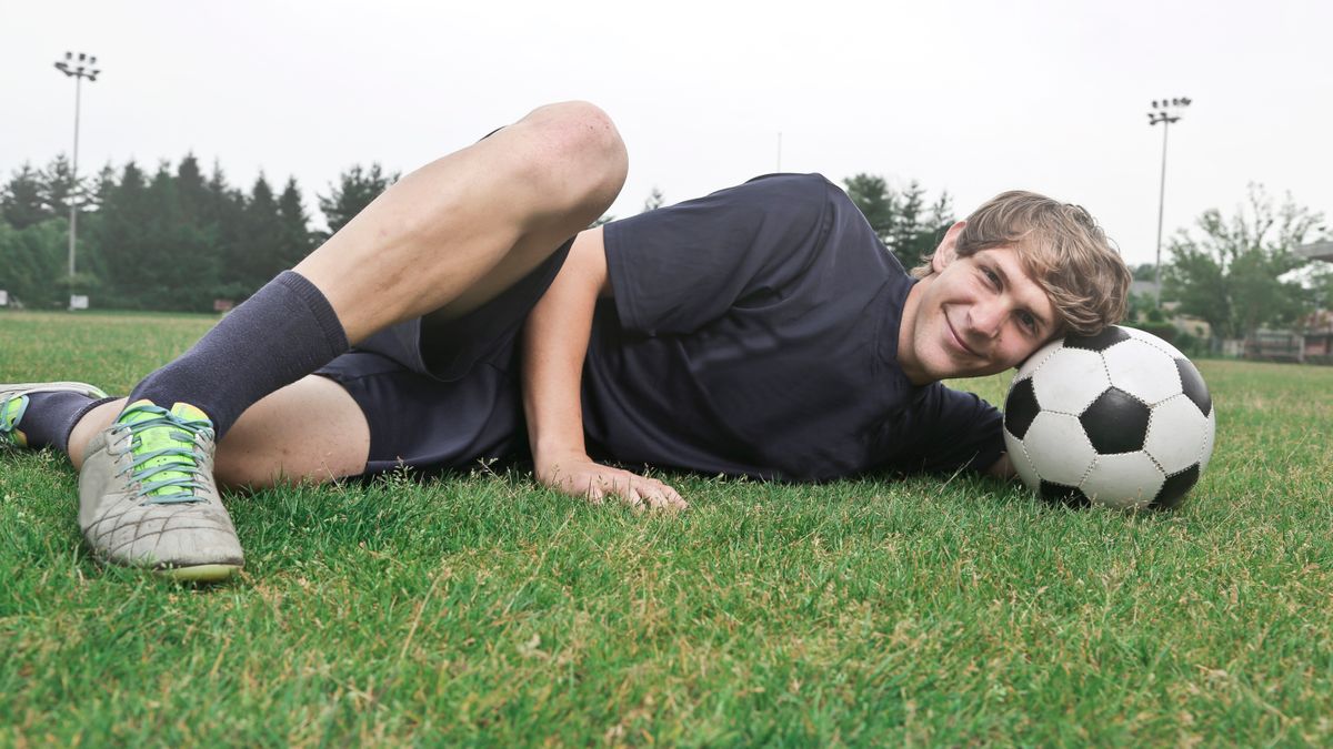 Teen soccer player smiling on grass field resting with a soccer ball. Teen soccer player smiling on grass field resting with a soccer ball.