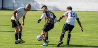 Three male soccer players actively competing on a sunny field.
