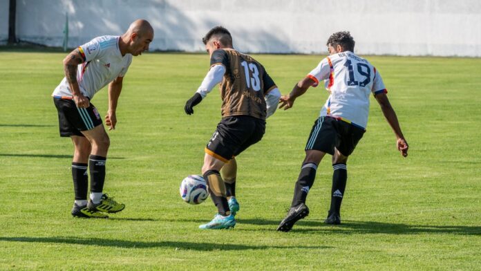 Three male soccer players actively competing on a sunny field.