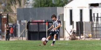 Dynamic action shot of a young male soccer player kicking a ball during a daytime match on an outdoor field.