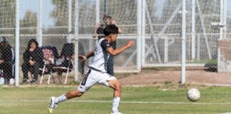 A dynamic image of a young male soccer player running and kicking a soccer ball during a game.
