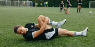 A female soccer player lying on the field, holding her injured leg in pain during a game.