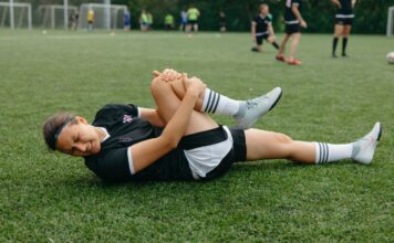 A female soccer player lying on the field, holding her injured leg in pain during a game.