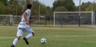 Soccer player in action dribbling a ball towards the goal on an outdoor field.