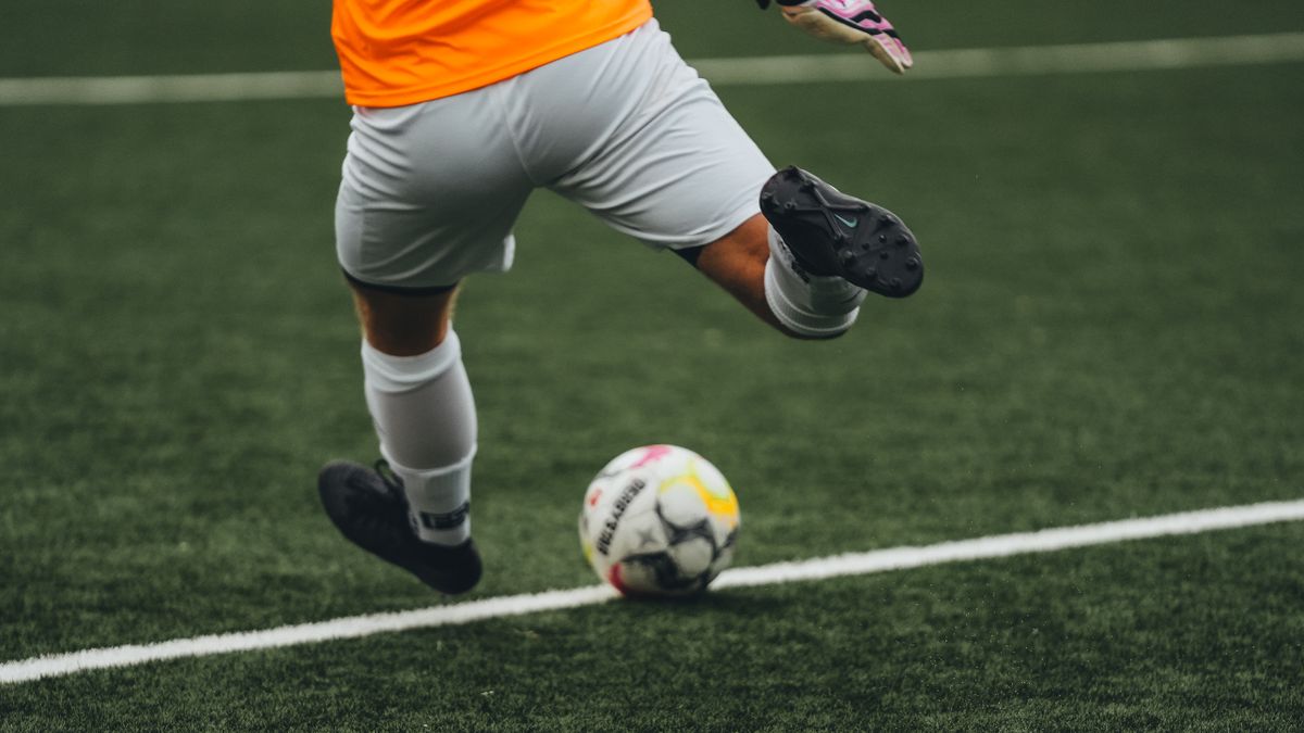 Dynamic shot of a soccer player kicking the ball during a game on a grass field. Dynamic shot of a soccer player kicking the ball during a game on a grass field.