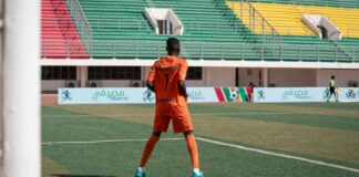 Soccer player in orange uniform on colorful stadium field during daytime game.