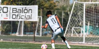 Action shot of a soccer player dribbling on a sunny outdoor field, showcasing athletic movement.