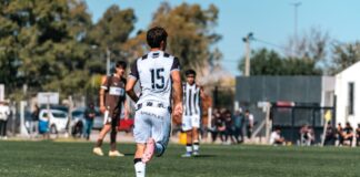 Back view of a soccer player with jersey number 15 running on a green field during a match.