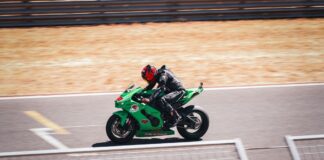 Motorcyclist on a green sportbike speeding on a sunny racetrack, showcasing speed and adrenaline.