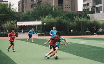 Players compete in an amateur soccer match on an urban field.