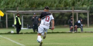 A teenager in soccer gear sprinting with the ball on a grassy field during a match.