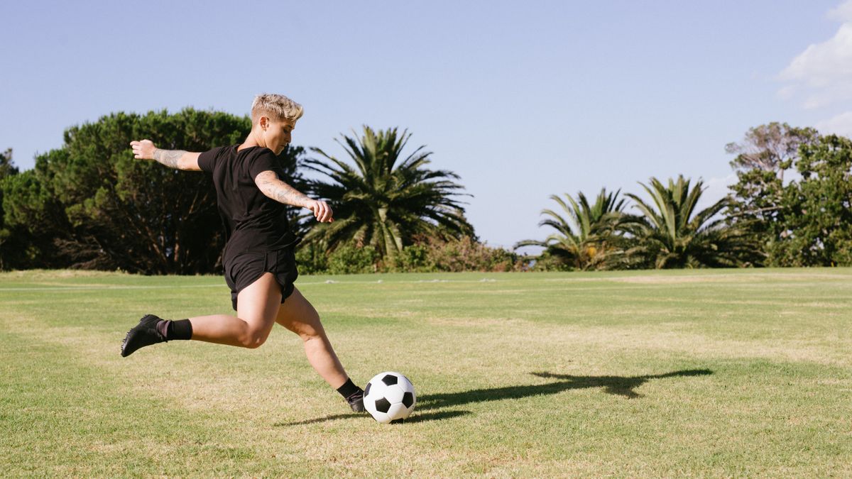 A woman soccer player kicking a ball on a grassy field during a sunny day outdoors. A woman soccer player kicking a ball on a grassy field during a sunny day outdoors.