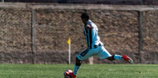 Soccer player in dynamic action kicking a ball on the field under bright sunlight.