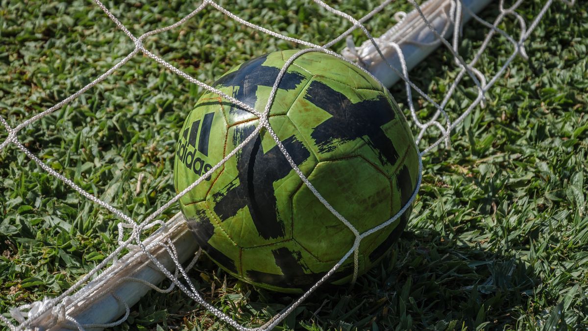Bright green soccer ball stuck in a net on a grassy field in sunlight. Bright green soccer ball stuck in a net on a grassy field in sunlight.