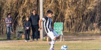 A young boy in a black and white jersey kicks a soccer ball during a match.