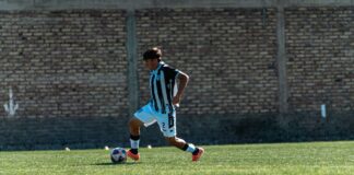 A teenage soccer player dribbles a ball during an outdoor match on a green field.