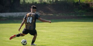 A soccer player prepares to kick the ball on a grassy field during daylight.
