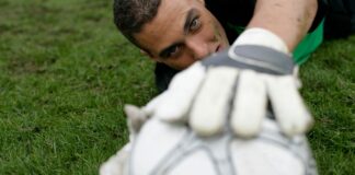 Dynamic shot of a goalkeeper reaching for a soccer ball on a grass field, showcasing sports dedication.