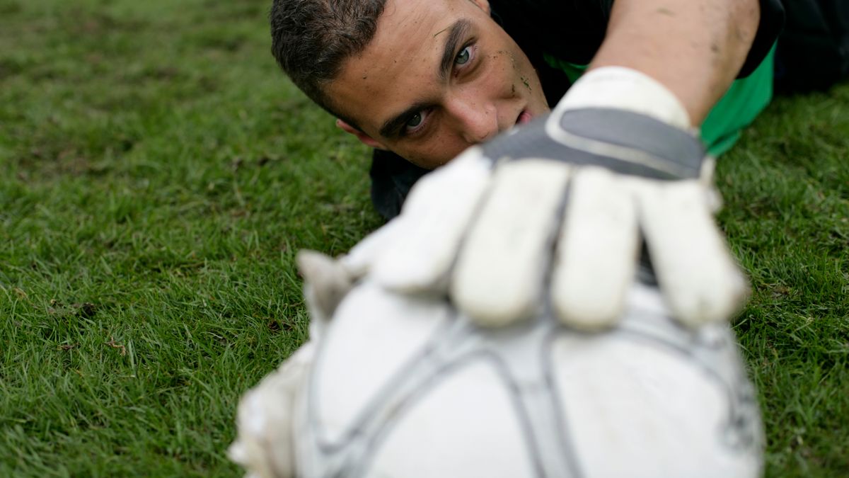 Dynamic shot of a goalkeeper reaching for a soccer ball on a grass field, showcasing sports dedication. Dynamic shot of a goalkeeper reaching for a soccer ball on a grass field, showcasing sports dedication.