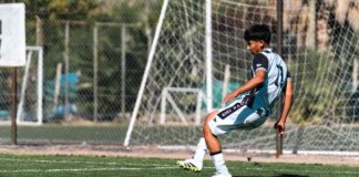 Teen football player kicks ball on sunny day outdoors, showcasing skill and athleticism in a match.