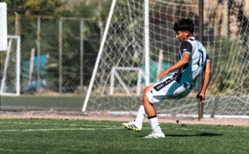 Teen football player kicks ball on sunny day outdoors, showcasing skill and athleticism in a match.