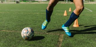 Dynamic image of a soccer player practicing drills on a grass field with vibrant shoes and cones.