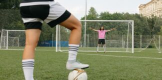 Soccer player in action aiming for the goal with a goalkeeper ready to defend.