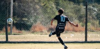 Youth soccer player in motion kicking a ball on a sunny outdoor field.