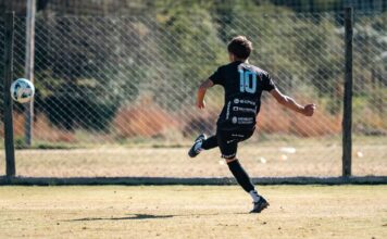 Youth soccer player in motion kicking a ball on a sunny outdoor field.