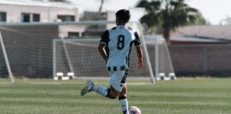 A young soccer player wearing a number 8 jersey runs with the ball on a sunny outdoor field.