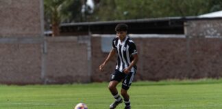 Young male soccer player dribbling on grassy field during a daytime match.