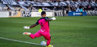 Goalkeeper in pink kit kicking the ball during a soccer match.