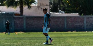 A soccer player stands on a sunny outdoor field during a game.