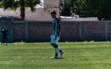 A soccer player stands on a sunny outdoor field during a game.