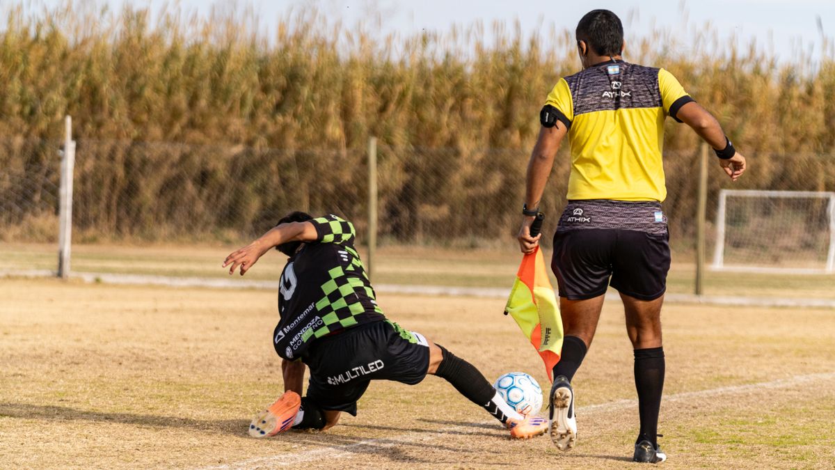 Soccer player tackles during a match as referee observes. Captured outdoors on a field. Soccer player tackles during a match as referee observes. Captured outdoors on a field.