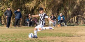 Young soccer player in action kicking the ball during a match with spectators in the background.