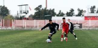 Three soccer players competing intensely on a grassy outdoor field.