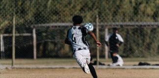 A young soccer player heads a ball during a game on a sunny outdoor field.