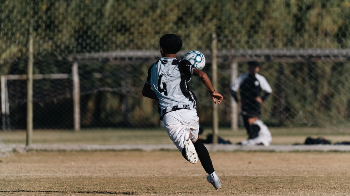 A young soccer player heads a ball during a game on a sunny outdoor field. A young soccer player heads a ball during a game on a sunny outdoor field.